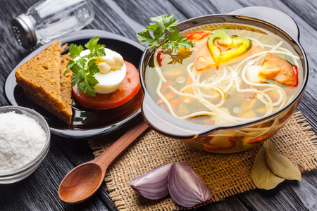 Fresh vegetable soup with noodles in a pot on the black wooden backgroundの写真素材