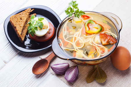 Fresh vegetable soup with noodles in a pot on the white wooden backgroundの写真素材
