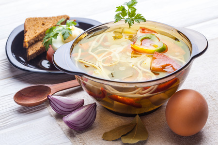 Fresh vegetable soup with noodles in a pot on the white wooden backgroundの写真素材
