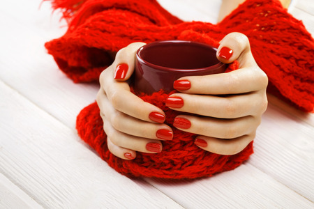 beautiful red manicure with a cup of tea on the white wooden table.の写真素材