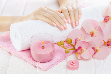 beautiful pink manicure with decor, orchid, towel and candle on the white wooden table. spaの写真素材