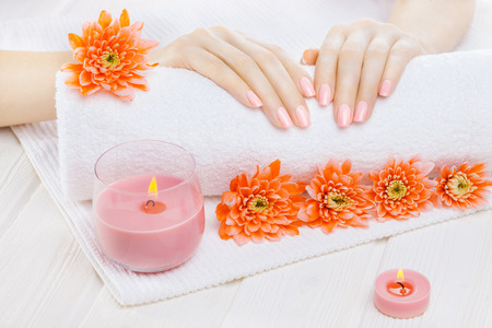beautiful pink manicure with orange chrysanthemum and towel on the white wooden table. spaの写真素材