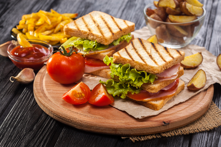 club sandwich with Tomato, lettuce, bacon, ham and french fries on the black wooden tableの写真素材