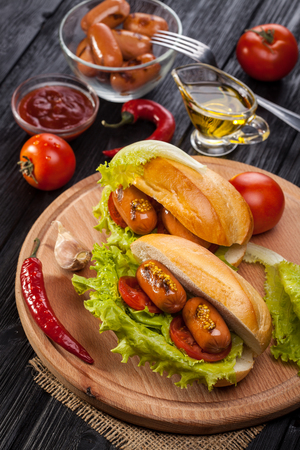 Hot dog with Tomato, lettuce, Sausage, mustard, ketchup on the black wooden tableの写真素材