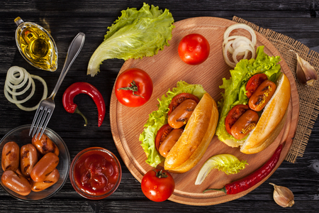 Hot dog with Tomato, lettuce, Sausage, mustard, ketchup on the black wooden table. Top viewの写真素材