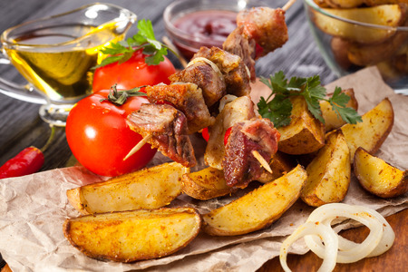 Meat skewer with herbs With onions, baked potatoes, tomatoes and greens on the black wooden tableの写真素材