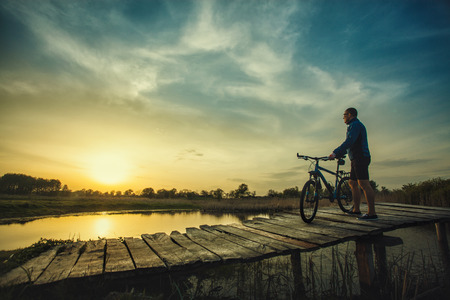 The cyclist admires the wonderful sunset on the bridgeの写真素材