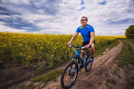 A male cyclist is riding on a picturesque yellow rapeseed field. Sports, active recreation.の写真素材