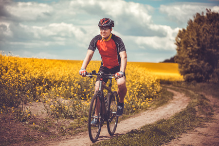 A male cyclist is riding on a picturesque yellow rapeseed field. Sports, active recreation.の写真素材