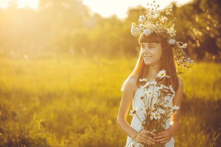 Happy little girl on a sunset meadow with a bouquet of flowering chamomilesの写真素材