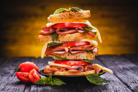 Club sandwich with cheese,basil, tomato, ham on the black wooden tableの写真素材