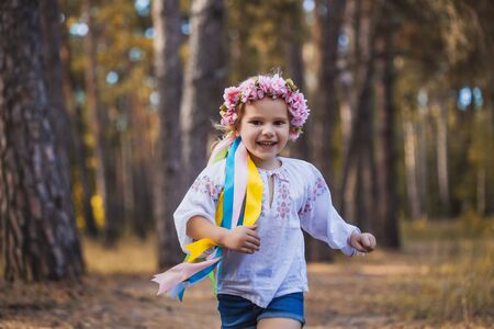 A little girl in a wreath with ribbons is running happily through the summer forest.の写真素材