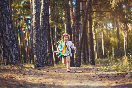 A little girl in a wreath with ribbons is running happily through the summer forest.の写真素材