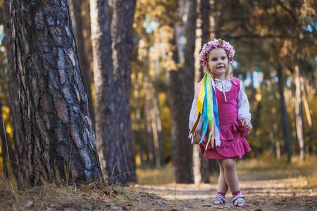 A little girl in a wreath with ribbons is running happily through the summer forest.の写真素材