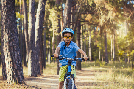 kid on a bicycle in the sunny forest. boy cycling outdoors in helmetの写真素材