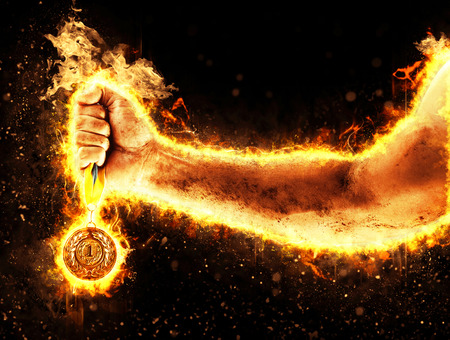 Mans hand in a fire is holding up gold medal. Winner in a competition.の写真素材