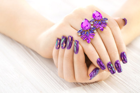 beautiful purple manicure with earrings on the white wooden table.の写真素材