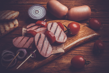 skewers of grilled sausages with tomatoes onions, croutons on the old wooden tableの写真素材