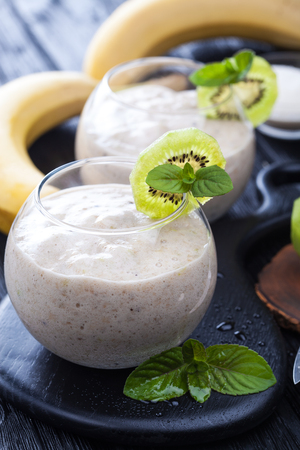 fresh banana smoothie with apple, kiwi and mint on a black wooden table.の写真素材