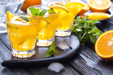 orange cocktail with ice and fresh mint on a black wooden tableの写真素材