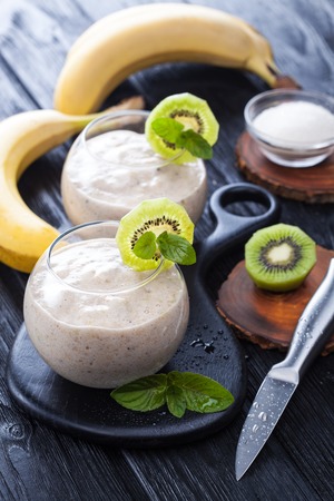 fresh banana smoothie with apple, kiwi and mint on a black wooden table. delicious and healthy breakfastの写真素材