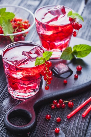 Red currant cocktail with ice and fresh mint on a black wooden tableの写真素材