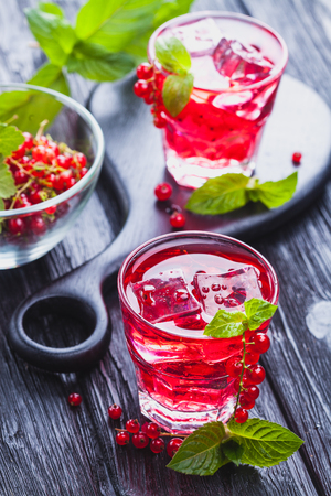 Red currant cocktail with ice and fresh mint on a black wooden tableの写真素材