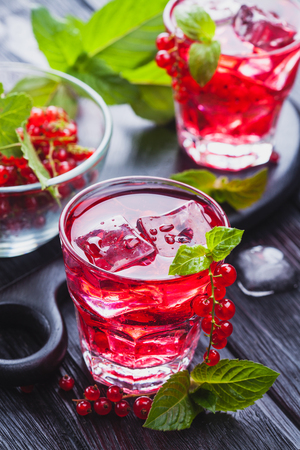 Red currant cocktail with ice and fresh mint on a black wooden tableの写真素材