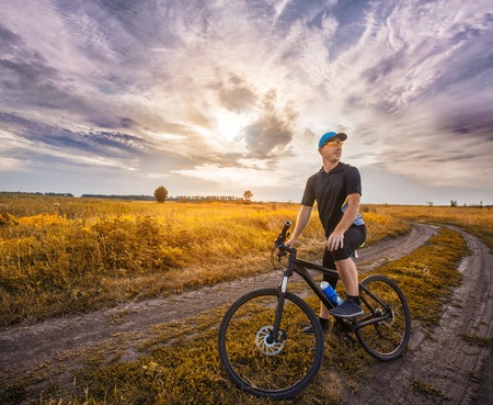 Happy man cyclist rides field road on a mountain bike on the Sunset.の写真素材