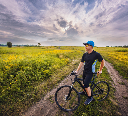Happy man cyclist rides field road on a mountain bike on the Sunset.の写真素材