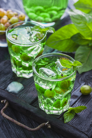 green gooseberry cocktail with ice and fresh mint on a black wooden tableの写真素材