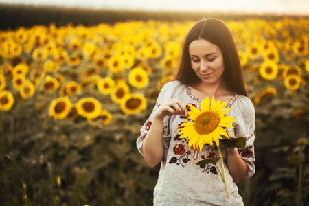 Cute brunette in a blossoming sunflower field in a national Ukrainian clothes. rural happy lifeの写真素材