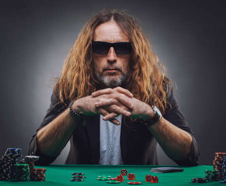 Long-haired handsome man playing poker in a casino. Studio concept on gray backgroundの写真素材