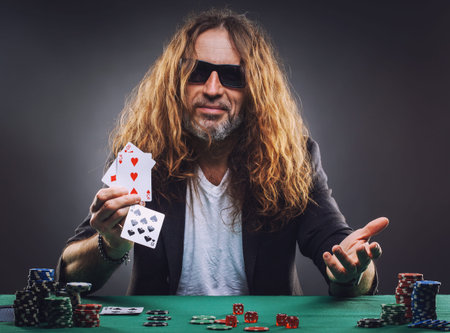 Long-haired handsome man playing poker in a casino. Studio concept on gray background