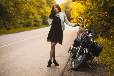 attractive brunette motorcyclist standing near a motorcycle On the Sunset.の写真素材