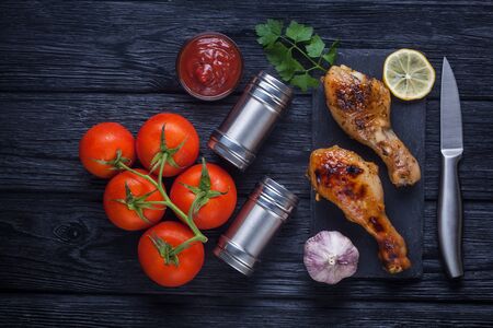 chicken legs with tomatoes, lemon, parsley and ketchup on a black slate boardの写真素材
