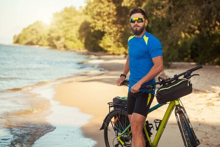 bearded man cyclist rides along the sandy beach on a mountain bike.の写真素材