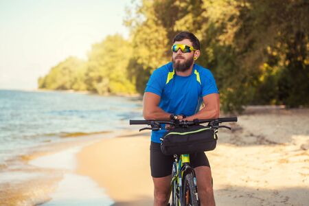 bearded man cyclist rides along the sandy beach on a mountain bike.の写真素材