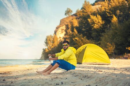 bearded man resting with a tent on a sandy beach.の写真素材