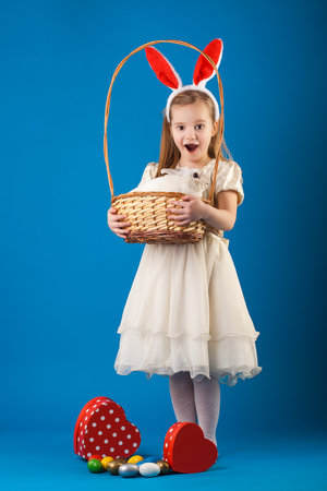 Cute girl with White rabbit in basket with Easter eggs on the blue backgroundの写真素材