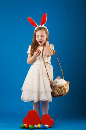 Cute girl with White rabbit in basket with Easter eggs on the blue backgroundの写真素材