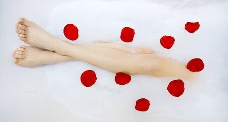Legs of beautiful young female in bath tub with liquid soap and rose petalsの写真素材