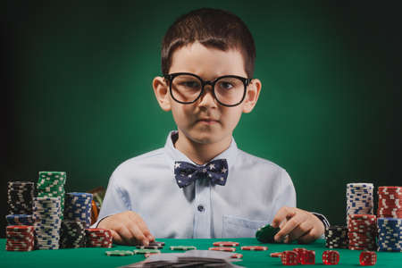 Little kid playing poker in a casino. Studio concept on blue backgroundの写真素材