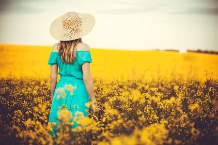 Young woman standing on the rape field with sunrise on the backgroundの写真素材