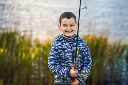 Cute boy catches fish on a summer lake.の写真素材