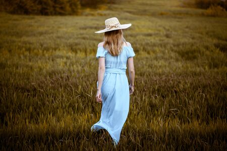Young woman standing on a wheat field with sunrise on the backgroundの写真素材
