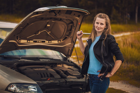 Worried young woman with her broken car with a wrench in her hand