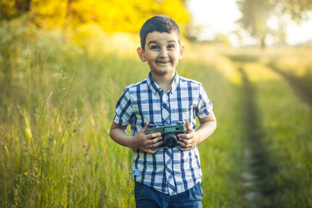 Beautiful smiling kid boy holding a retro DSLR camera in the park
