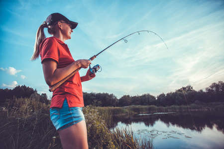 Cute woman is fishing with rod on lakeの写真素材