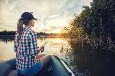 Cute woman is fishing with rod on a summer lakeの写真素材